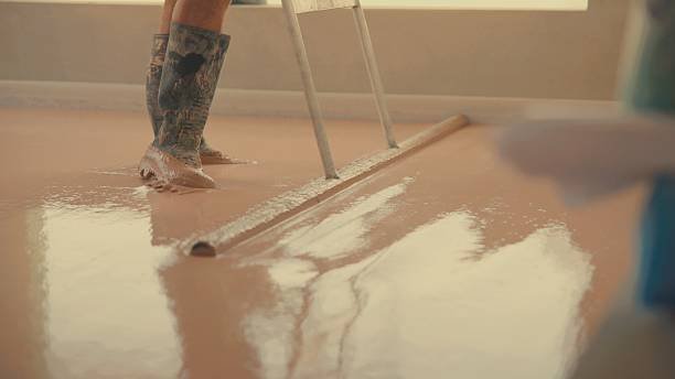 Construction worker leveling liquid gypsum screed on a floor
